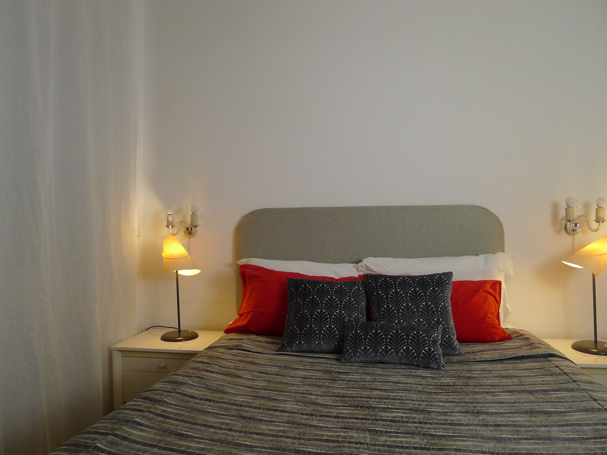 Een opgemaakt bed met een gestreept beddegoed, twee bedlampen en een hoofdbord met een grijze bovenkant.