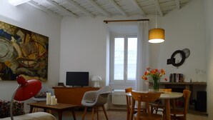A cozy living room with a TV, a painting, a dining table with chairs, a red desk lamp, and a bookshelf with books and glasses. - Via Crispi Spanish Steps Apartment. New right in the central elegant and quiet (Roma)
