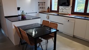 Et kompakt køkken med en sort bordplade, hvide skabe og et spiseområde med fletstole.