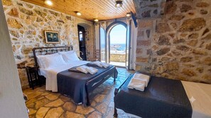 A bedroom with a stone wall, a bed, a bench, and a view of the sea. - Four Seasons Stonework Castle (saronida)