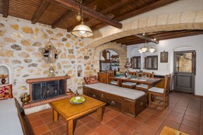 A rustic stone-walled room with a fireplace, wooden furniture, and a tiled floor. - Four Seasons Stonework Castle (saronida)