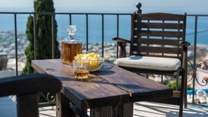 Une table en bois avec une bouteille et des verres, un bol de chips, et une chaise sur un balcon donnant sur la ville.