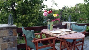 An outdoor wooden table set with plates, cutlery, and a vase of flowers.