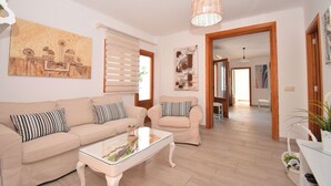 Una sala de estar con un sofá color beige, una mesa de centro de vidrio y obras de arte en las paredes.