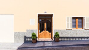 Un edificio con una puerta doble de madera, una ventana pequeña con contraventanas y dos macetas en el suelo.