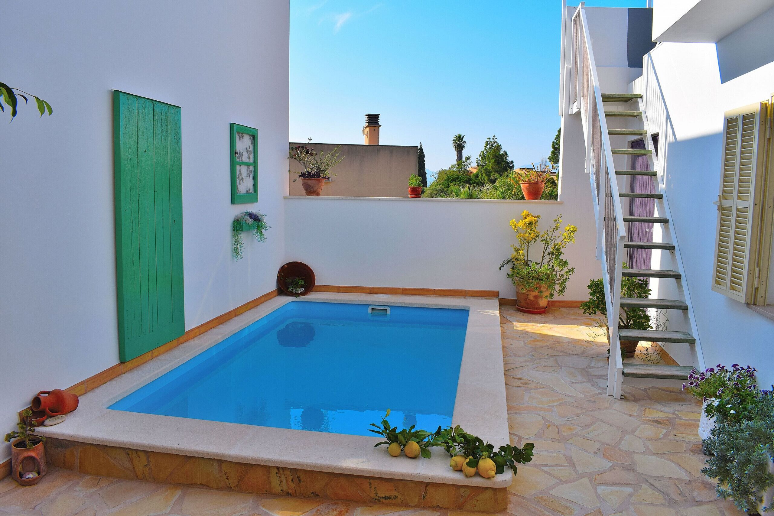Uma pequena piscina ao ar livre com piso de pedra, rodeada por plantas em vasos e uma escadaria que dá acesso a um nível superior.