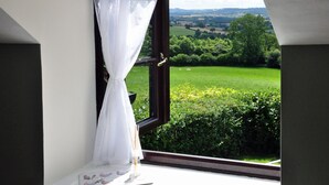 Habitació amb un finestral gran, cortines blanques i vistes a un paisatge verd.