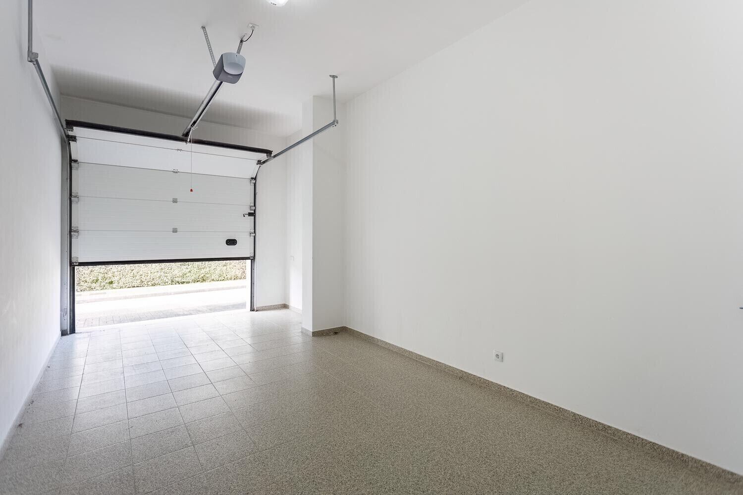 Een schone, lege garage met betegelde vloer en een garagepoort.