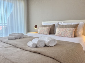 Una cama bien hecha con toallas enrolladas, una lámpara de noche y almohadas estampadas.