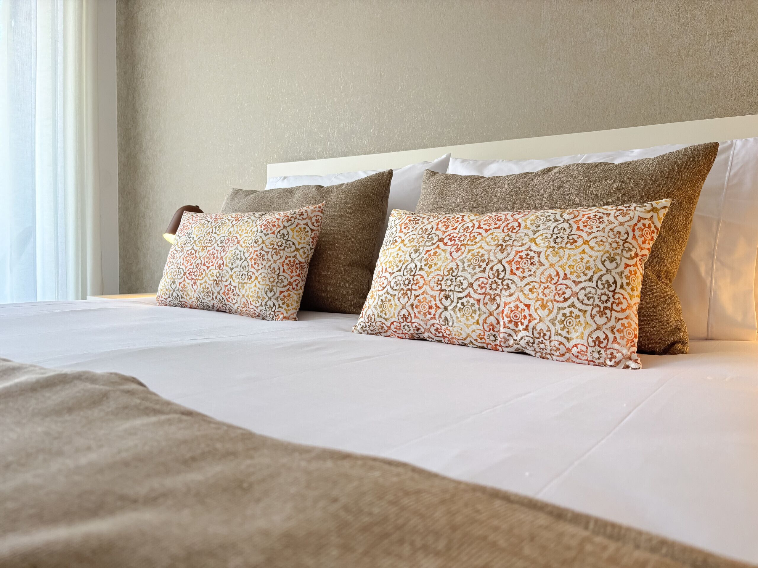 A neatly made bed with patterned pillows and a plain headboard.