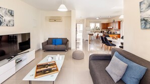 A modern living room with a flat-screen TV, a coffee table, a sofa, and a dining area with chairs.
