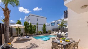 A poolside area with lounge chairs, a table with fruits, and a clear blue sky.