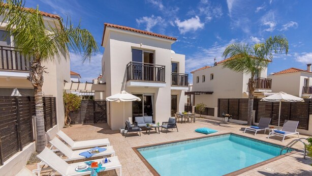 A two-story building with a swimming pool, outdoor seating, and palm trees.