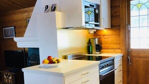 Een keuken met witte kastjes, een ingebouwde oven en een magnetron. Op het aanrecht staat een fruitschaal en er ligt een tapijt met een patroon op de vloer.