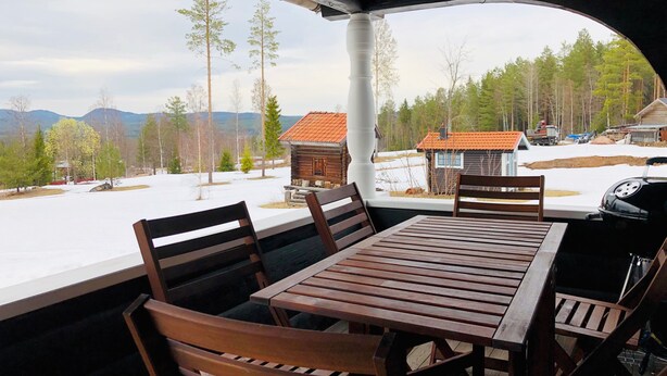 Een overdekt terras met een tafel en stoelen, met uitzicht op een besneeerd landschap met bomen en gebouwen.