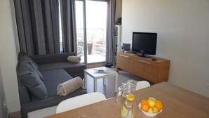 Una sala moderna con un sofá, una mesa de centro, un televisor y una mesa de comedor con un frutero.