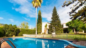 Une piscine dotée d’une terrasse carrelée, entourée d’une clôture et de différents arbres.