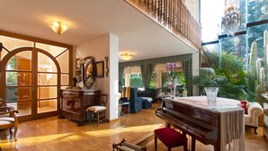 Un vaste salon agrémenté d’un magnifique piano à queue, d’un escalier en bois et d’une grande fenêtre donnant sur un jardin.