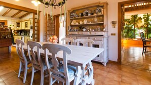 Un coin repas avec une table et des chaises en bois, un lustre et une cuisine en arrière-plan.