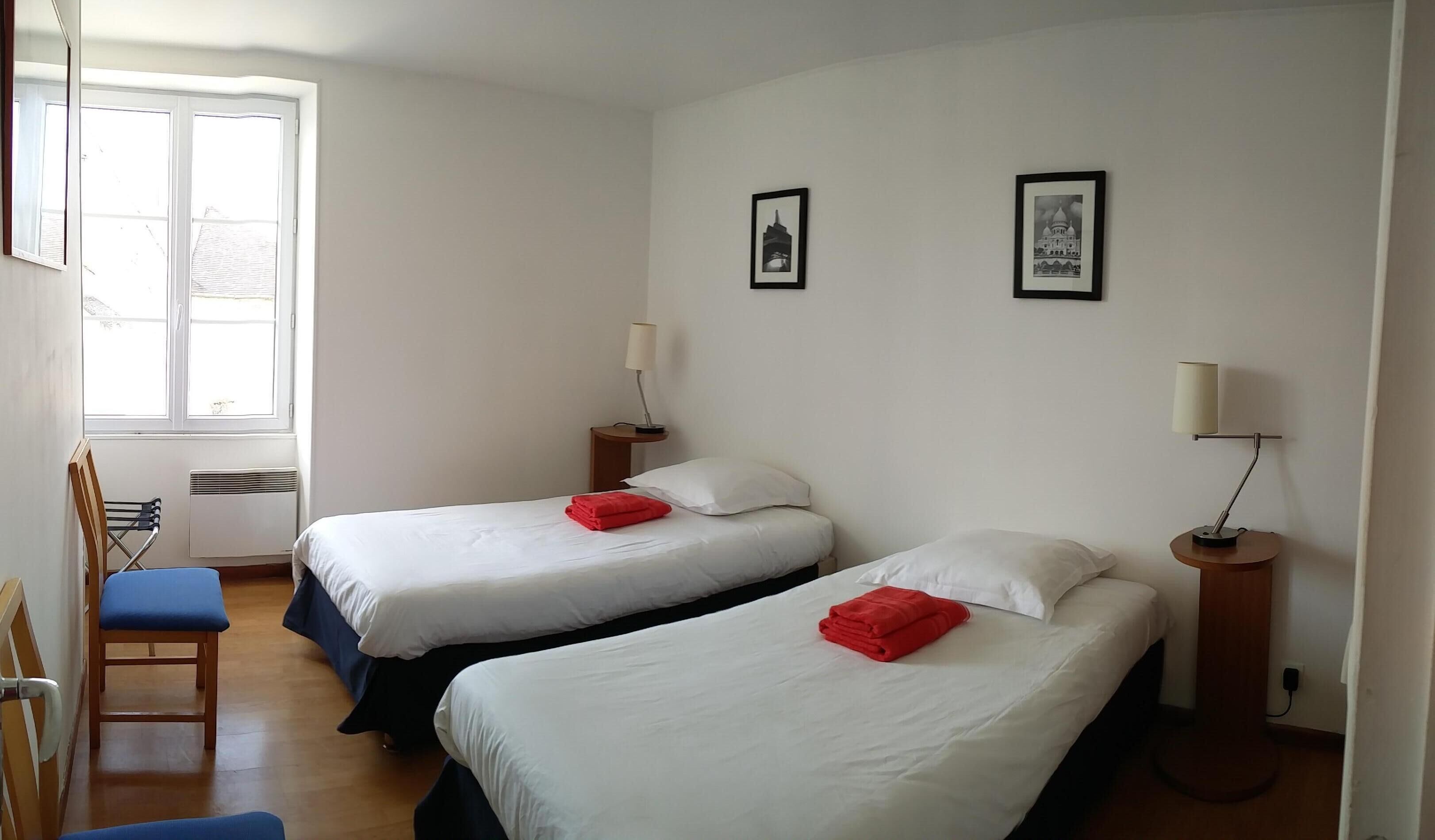 Habitación de hotel con dos camas, una silla, un ventanal y dos lámparas fijadas a la pared.