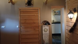 A wooden door with a clock and a sign that reads "TAKE TIME" in a room with wooden walls, a kitchen in the background, and two mounted deer heads on the wall. - Romantic Cottage; hier kom je tot rust! (Ulft)