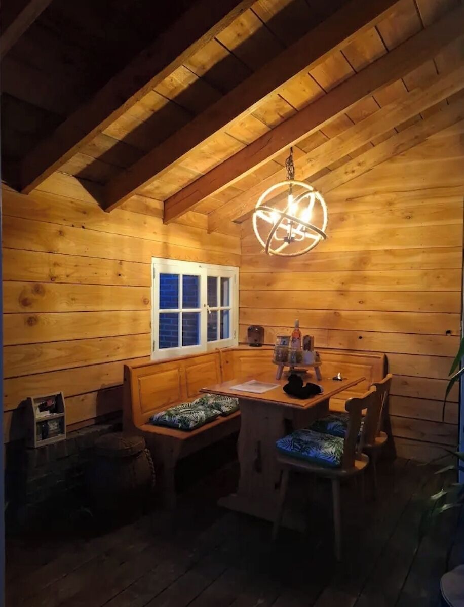 A cozy cabin interior with a wooden ceiling, a bench, a table, and a hanging light fixture.