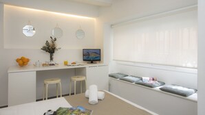Una habitación moderna y bien iluminada con un escritorio, dos taburetes, un televisor y una ventana con vistas.
