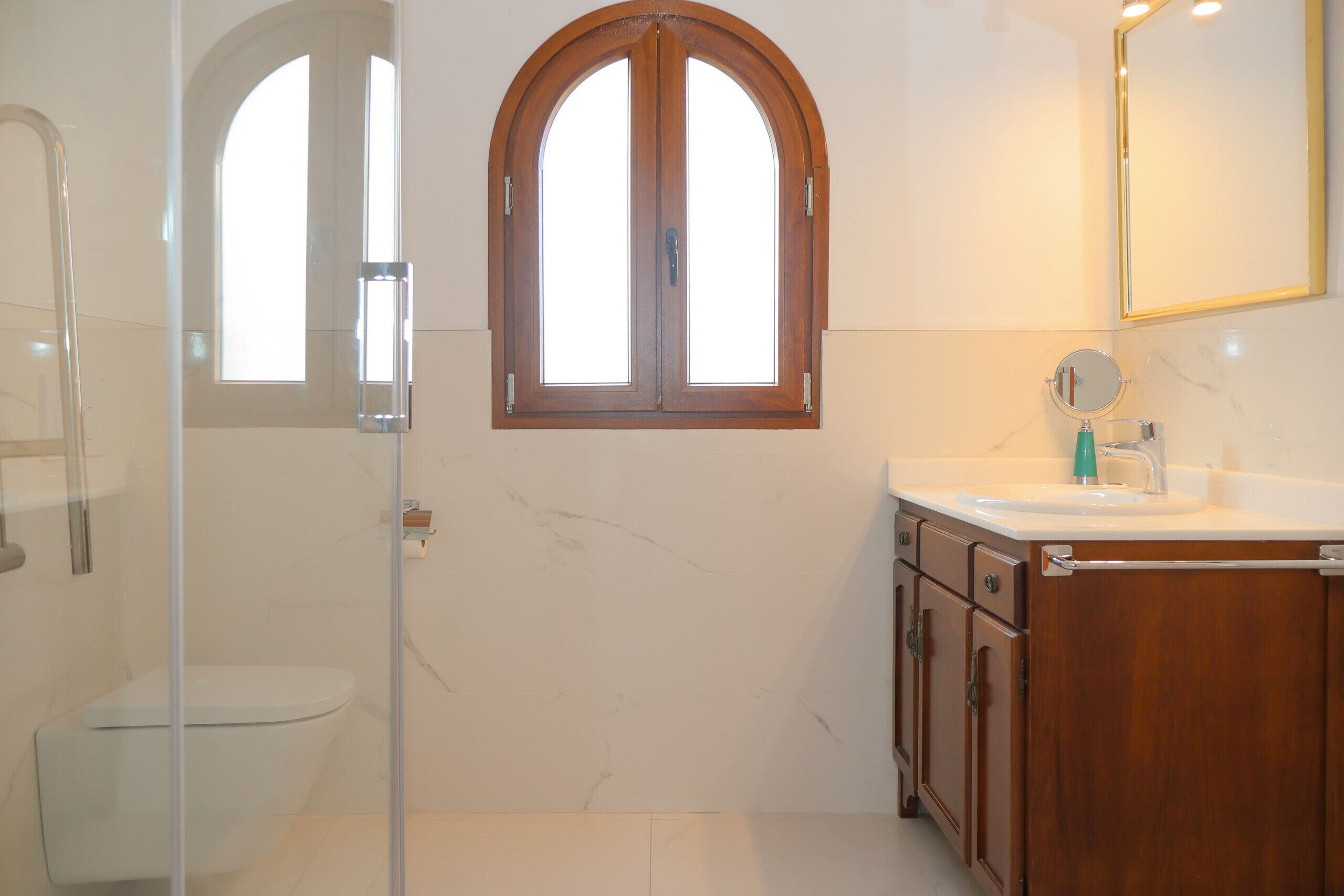 A bathroom with a toilet, shower, vanity, and a large arched window.