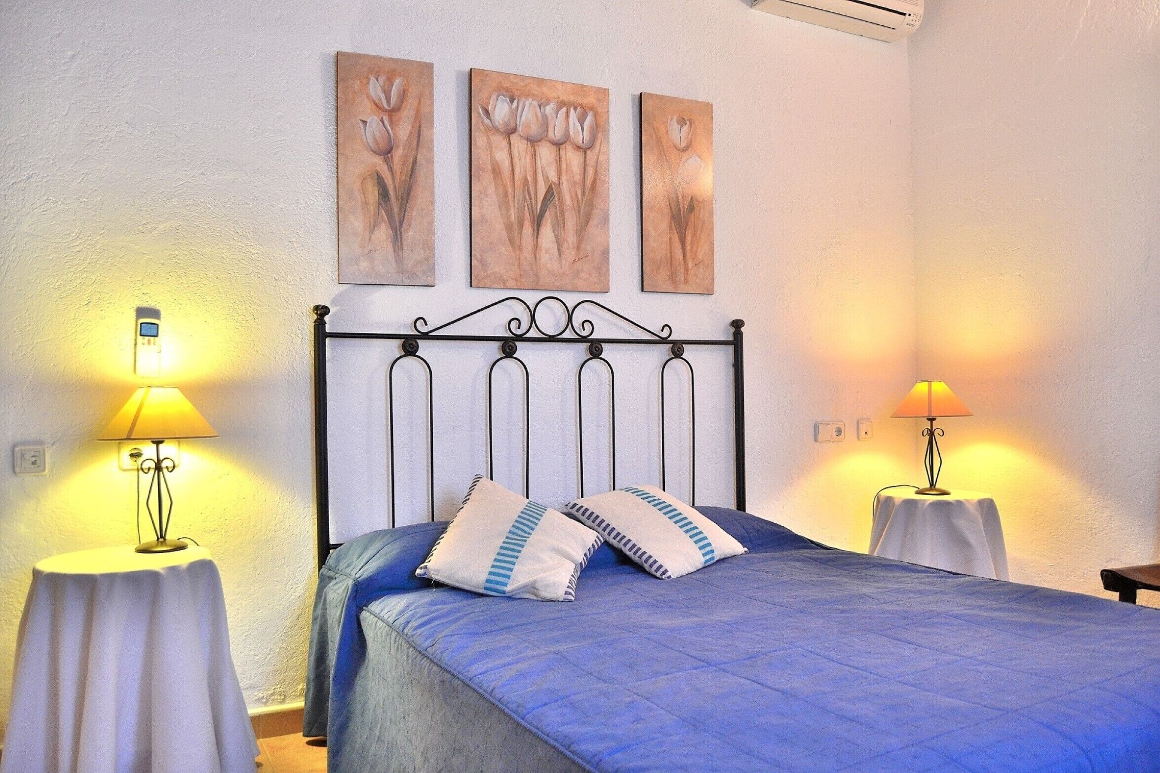 A bedroom with a bed, two bedside tables, and three wall-mounted paintings.