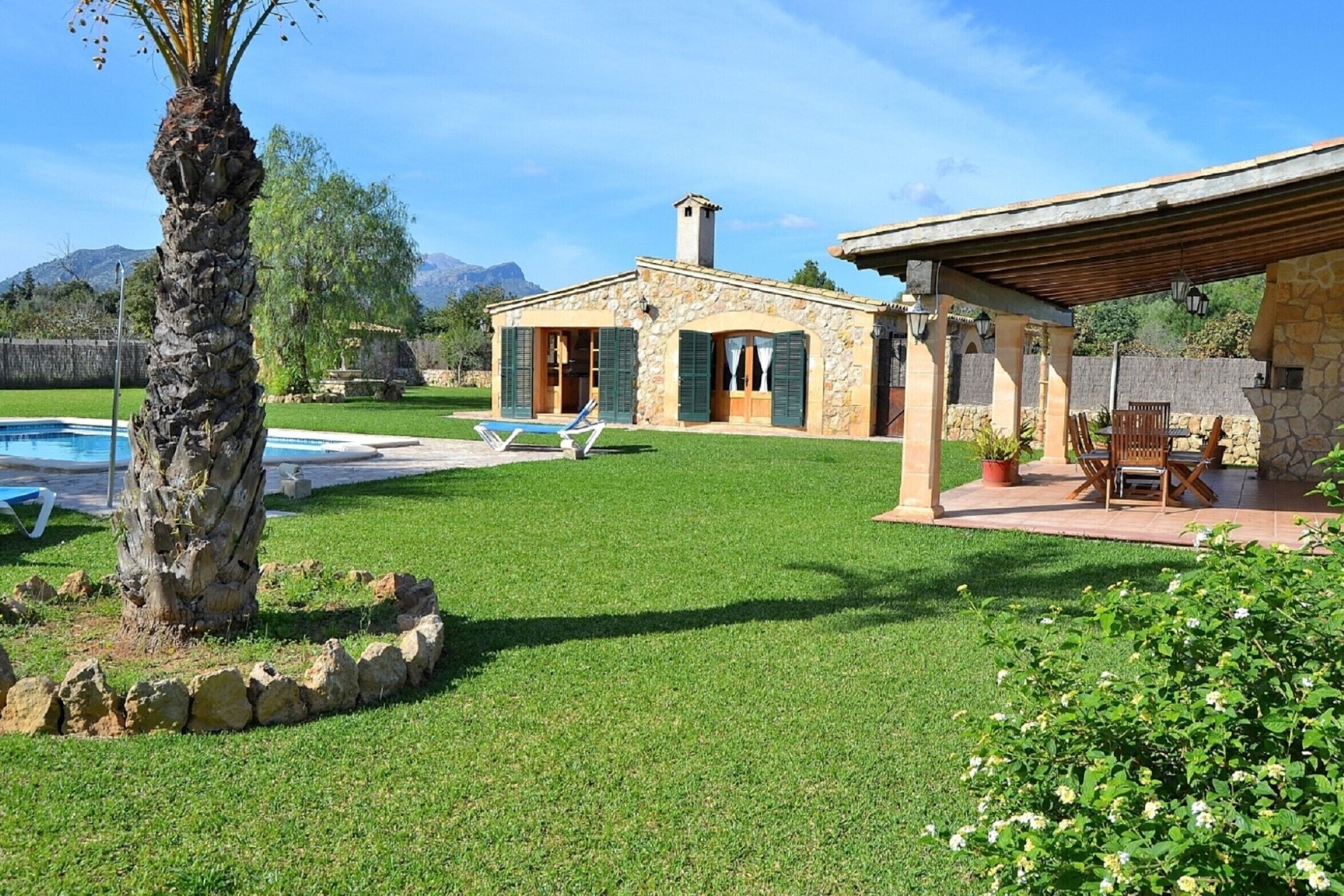 A stone house with a pool, green lawn, and a patio with outdoor furniture.