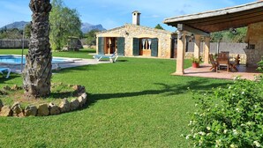 A stone house with a pool, green lawn, and a patio with outdoor furniture. - Can Roig Gran 041 magnificent finca with private pool, large barbecue area and WiFi (Pollensa / Pollença)