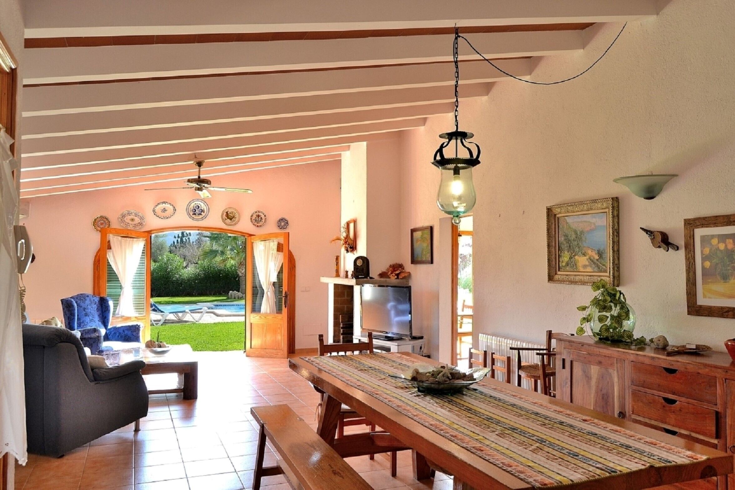 Un'ampia zona giorno con un grande tavolo da pranzo in legno, comodi posti a sedere e vista su un giardino tramite porte in vetro.