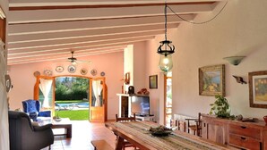 A spacious living area with a large wooden dining table, comfortable seating, and a view of a garden through glass doors. - Can Roig Gran 041 magnificent finca with private pool, large barbecue area and WiFi (Pollensa / Pollença)