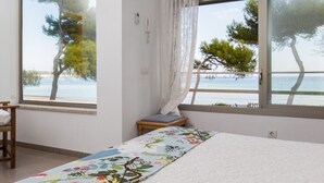 A bedroom with a bed, a chair, and a view of the sea through large windows. - Las Gaviotas - Spectacular beachfront villa with garden in Platja de Muro (Muro (Platja de Muro))
