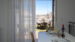 A dining area with a table set for two, a bottle of wine, and a view of a cityscape through a window.
