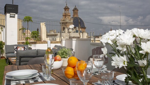 An outdoor dining area with a table set for two, a view of a historic building with a dome and bell towers, and a garden with white flowers.