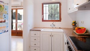 Een keuken met witte kasten, een raam met decoratieve ijzeren tralies, een spoelbak en een aanrecht met fruit.