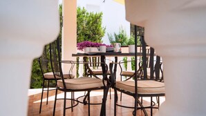 Een terras buiten met een ronde tafel en vier stoelen, omringd door potplanten en een gele parasol.