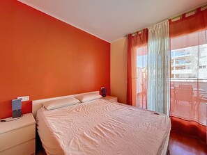 A bedroom with a bed, a nightstand, a lamp, and a window with curtains.