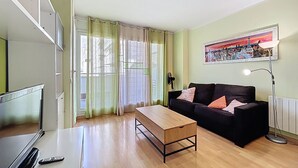 Ein Wohnzimmer mit einem Holztisch, einer schwarzen Couch mit Kissen, einem Fernseher und einem Bild an der Wand.
