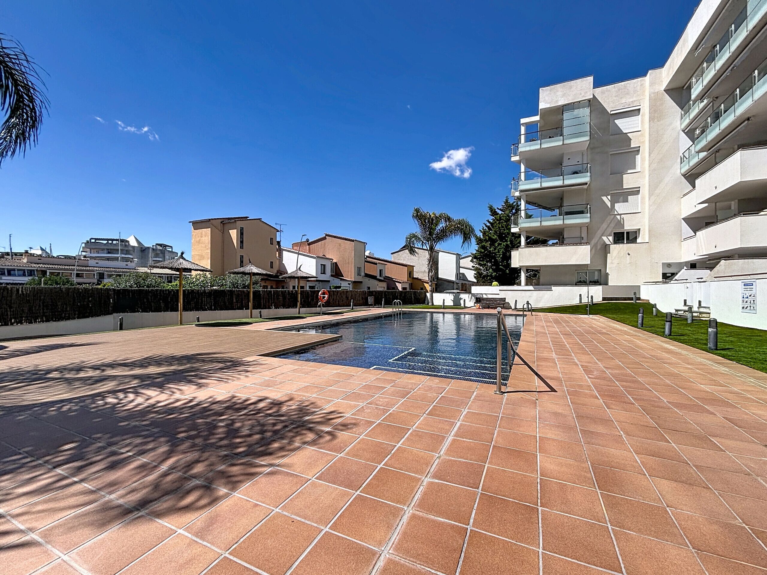 A swimming pool with tiled deck, surrounded by modern buildings and greenery.