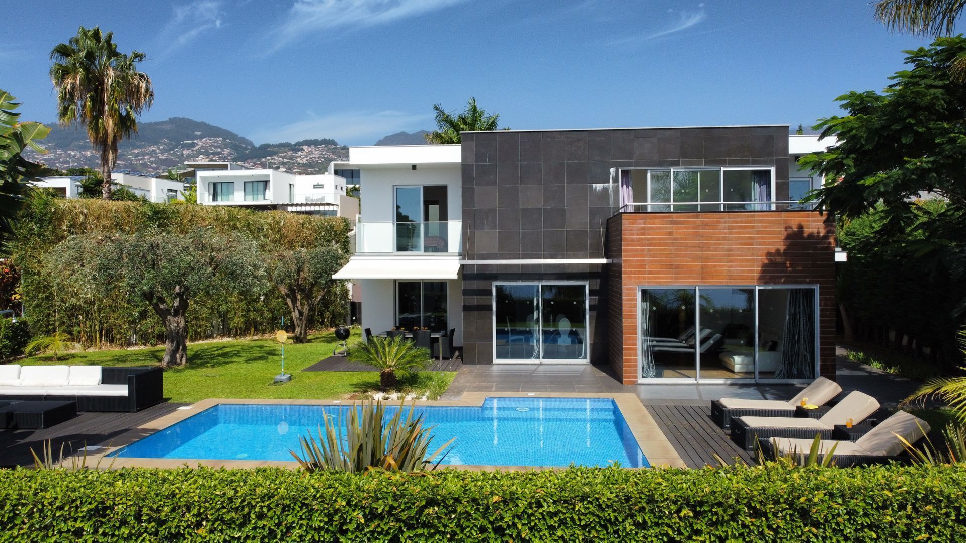A modern two-story house with a swimming pool, outdoor seating, and a view of the mountains.