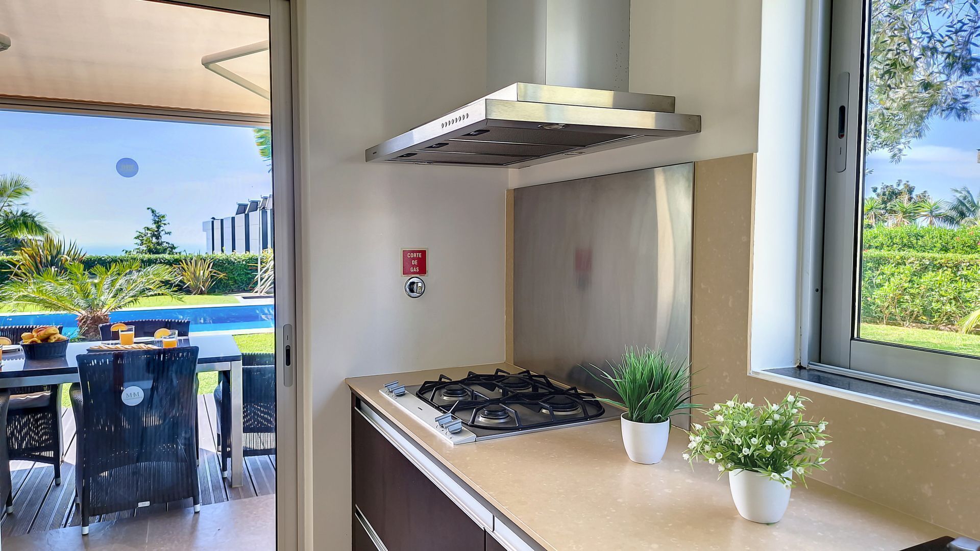 Cocina moderna con estufa a gas, campana de acero inoxidable y vistas a una piscina y zonas verdes.