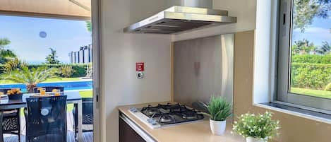 Cocina moderna con estufa a gas, campana de acero inoxidable y vistas a una piscina y zonas verdes.
