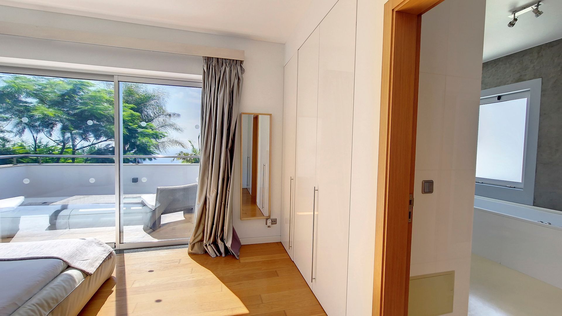 Et moderne soveværelse med en stor skydedør til en balkon, en seng med trægavl og et garderobeskab med spejl.