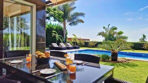 A poolside dining area with a view of a swimming pool, lounge chairs, and tropical vegetation. - Villa Ravenala by LovelyStay (Funchal)
