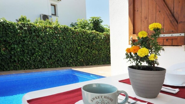 A poolside setting with a white table, a potted plant with yellow flowers, and a cup with "Sweet Home" text. - -Villa with private swimming-pool. HUTG-001429 (l'Escala)