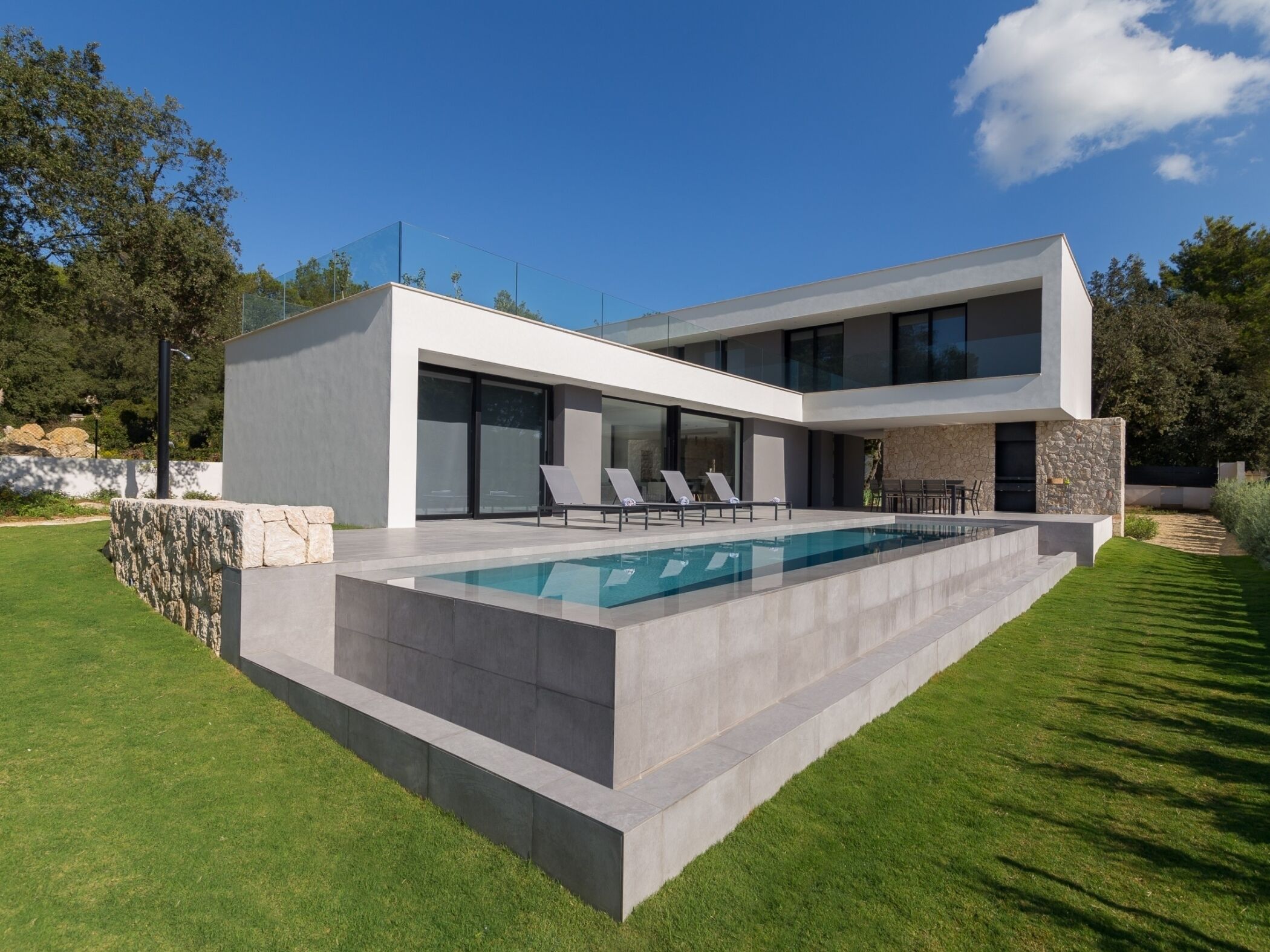 A modern two-story house with a swimming pool, outdoor seating, and a stone wall.