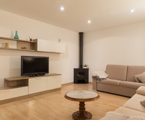 A modern living room with a flat-screen TV, a sofa, a round table, and a wood-burning stove. - Casa Lluna - Beautiful town house with pool in Campanet (Campanet)