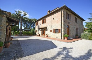 A stone building with a courtyard, featuring a gravel path, potted plants, and a pergola.